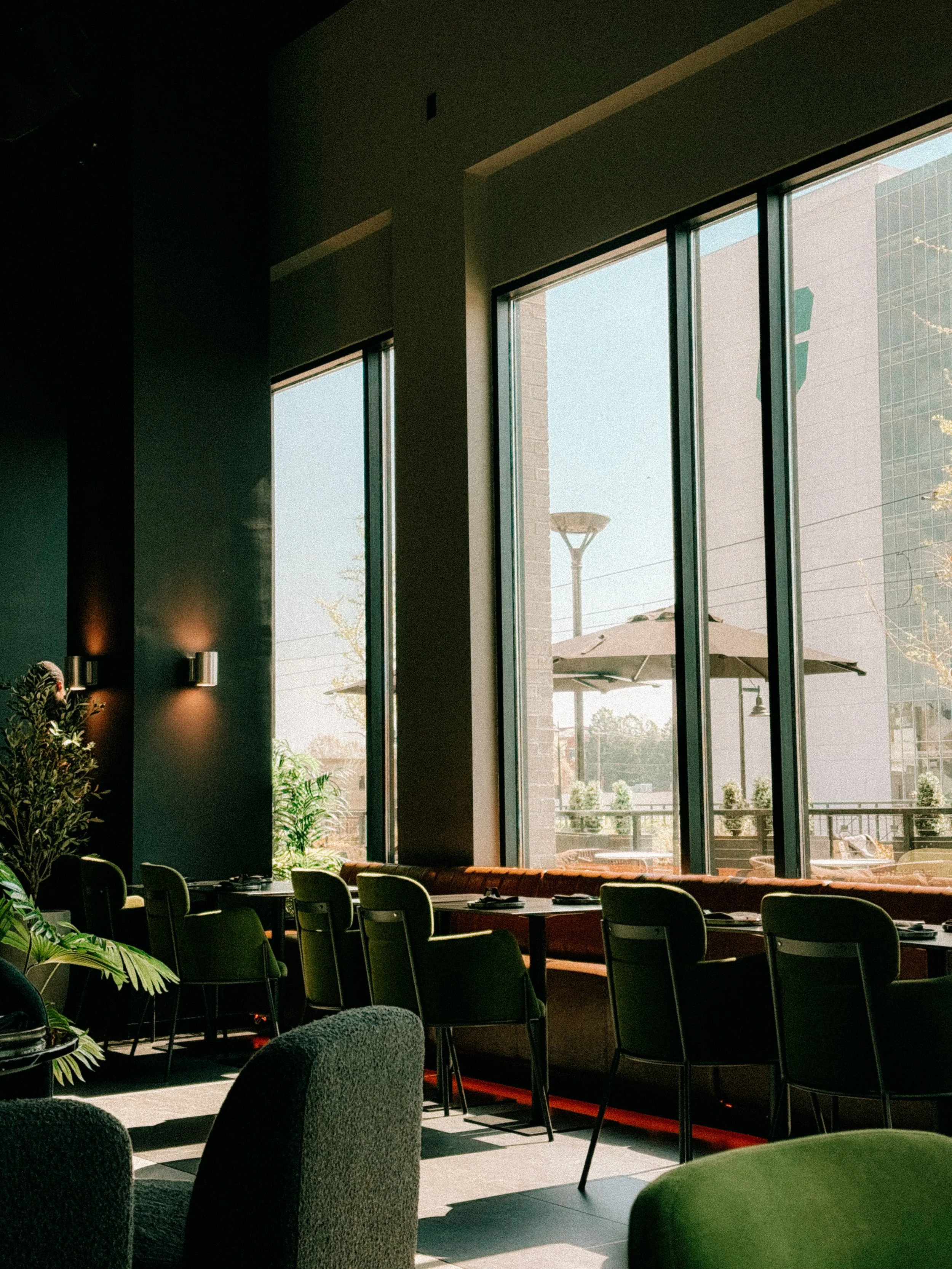 Interior of a restaurant with green velvet chairs looking out large windows towards a patio and a building in Charlotte, NC
