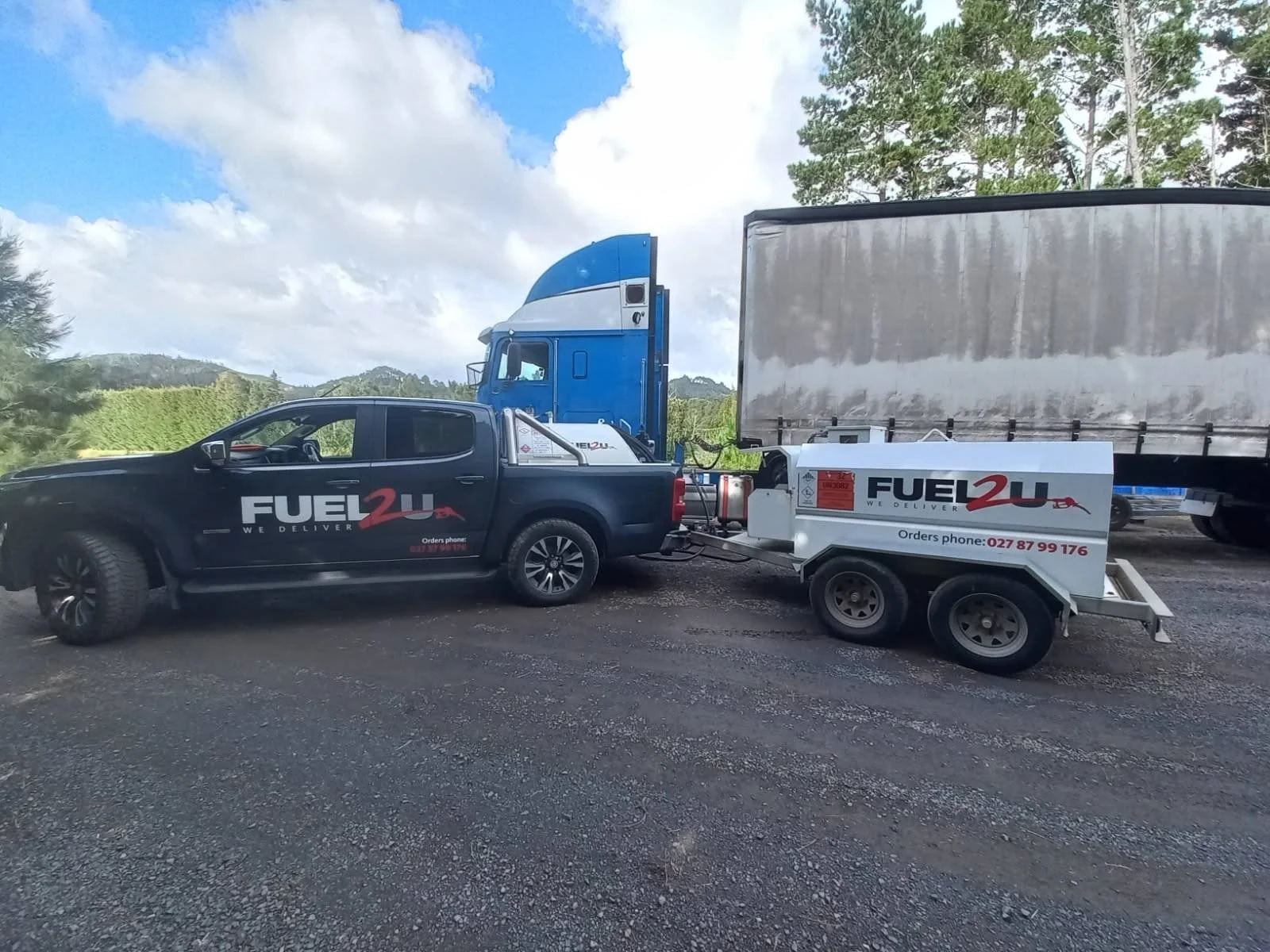 A black pickup truck with 'Fuel 2U' branding on the side, connected to a trailer that also has 'Fuel 2U' branding, in an outdoor setting with trees and cloudy sky in the background.