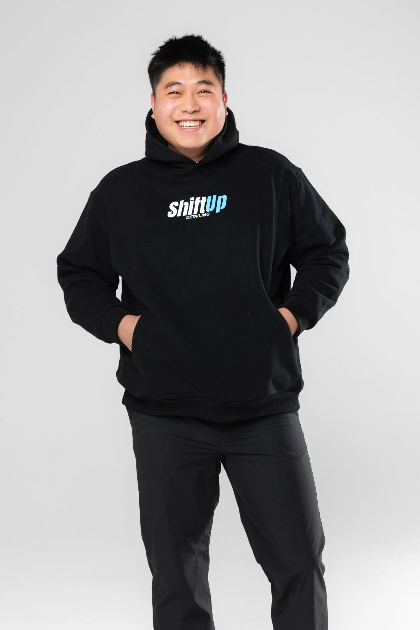 Chris zhang wearing a black hoodie with 'shiftup DETAILING' printed on it, standing against a plain white background.