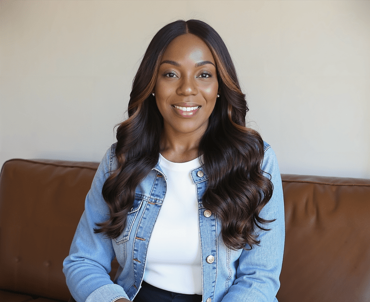 Dr. Sherrá Watkins seated, wearing a denim jacket over a white top, smiling at the camera.