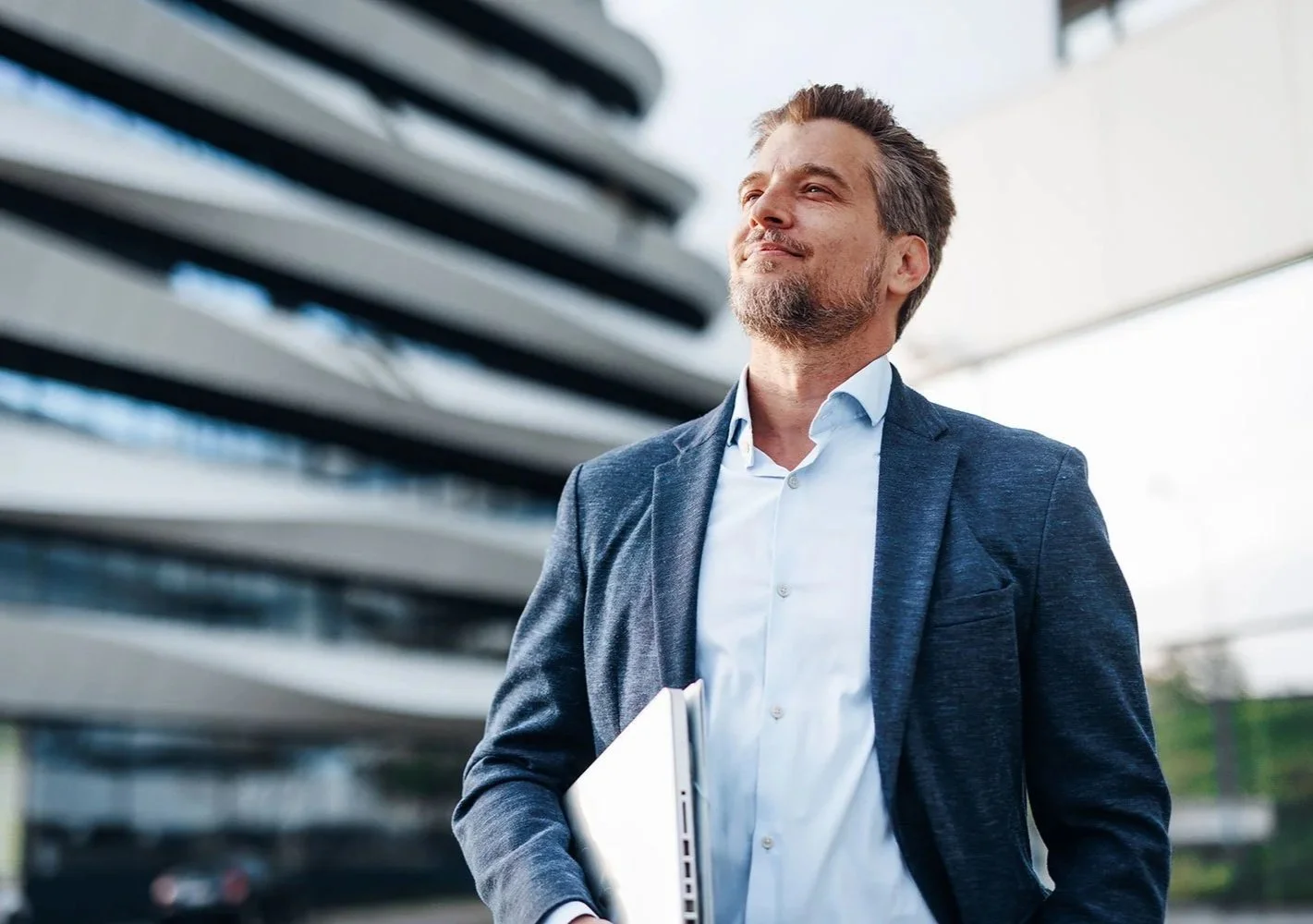 Confident businessman walking to next customer meeting, carrying a laptop and folder