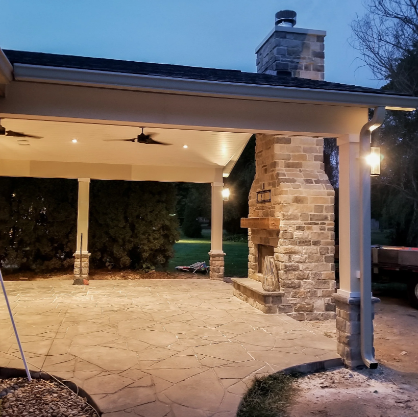 Custom porch with stone flooring, a brick fireplace, ceiling fans, and lighting fixtures.