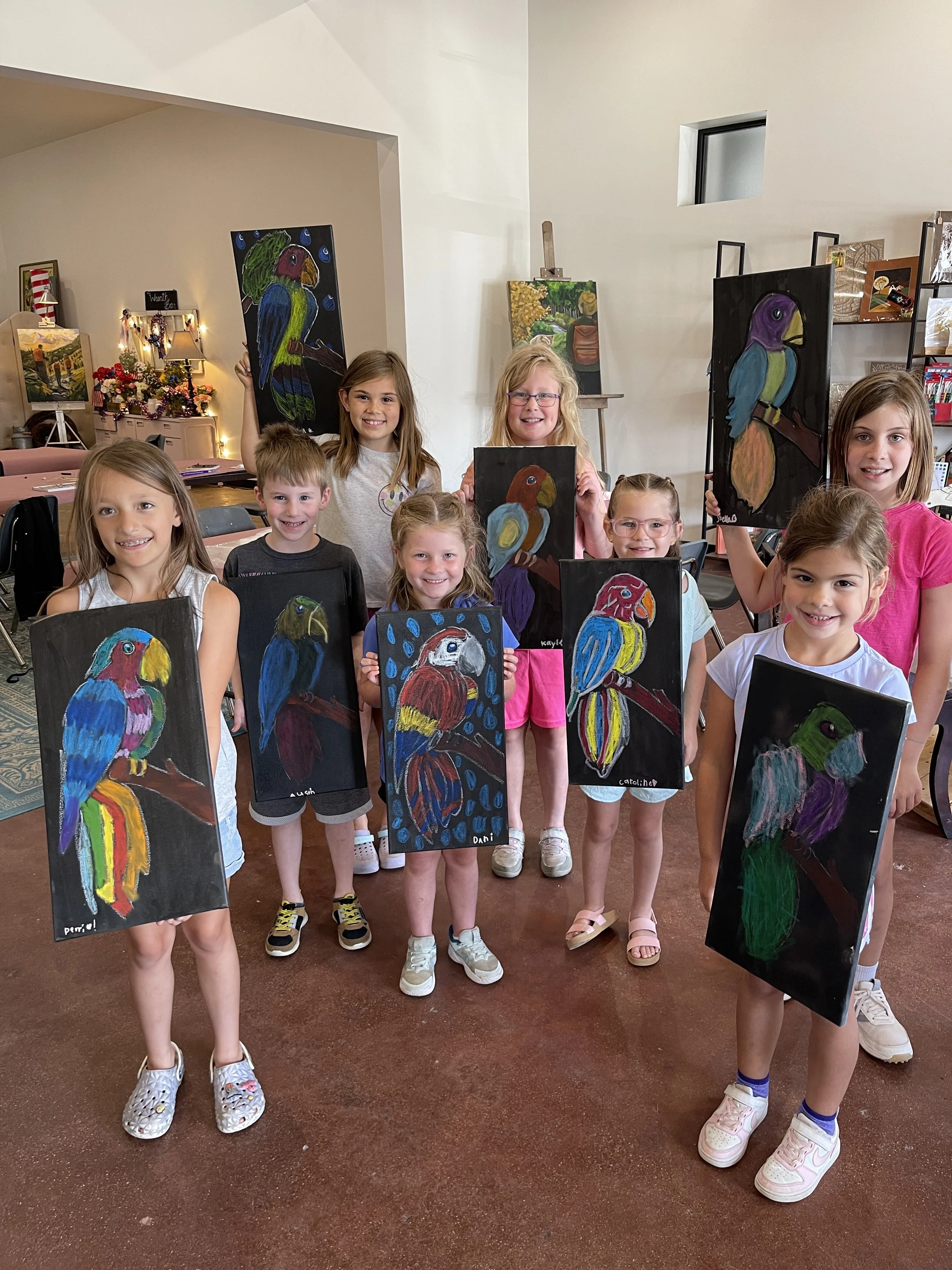 Group of young children holding colorful bird-themed paintings in an art studio.