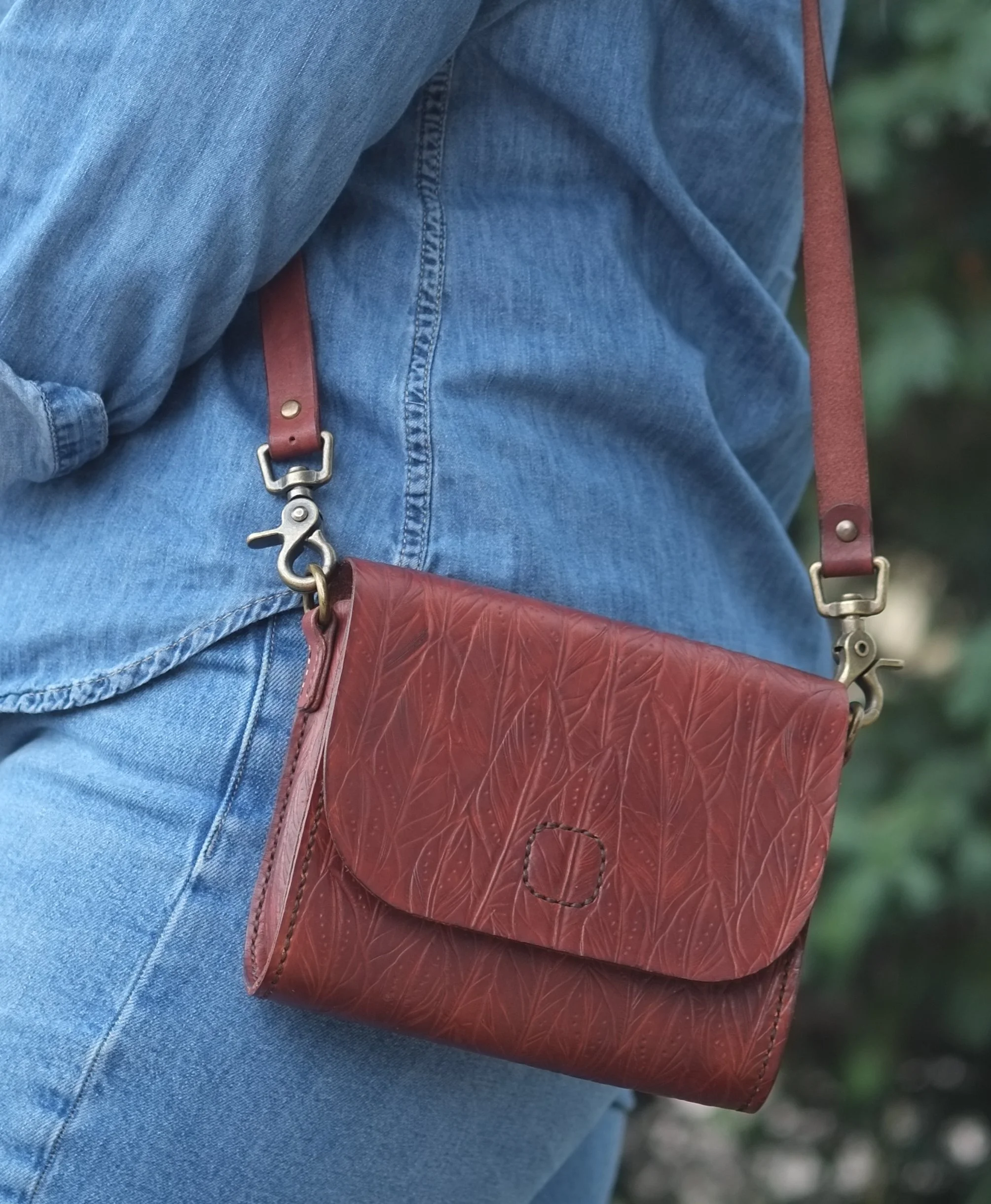 model holding small hand tooled brown leather handbag with feather pattern