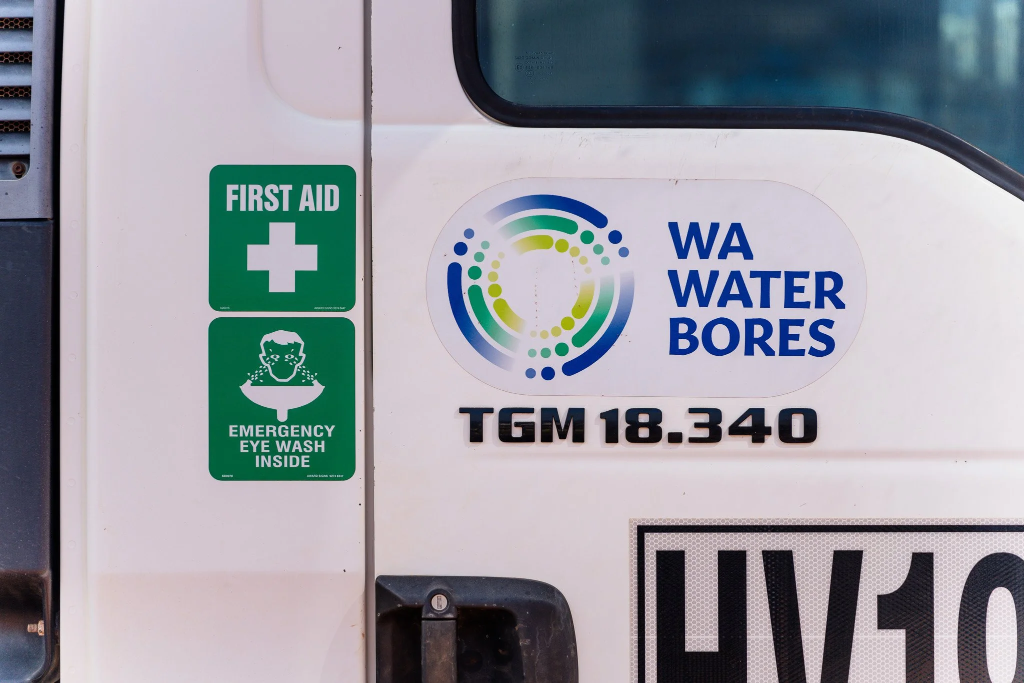Close-up of a vehicle door with WA Water Bores logo, a first aid sticker, and an emergency eye wash station label.