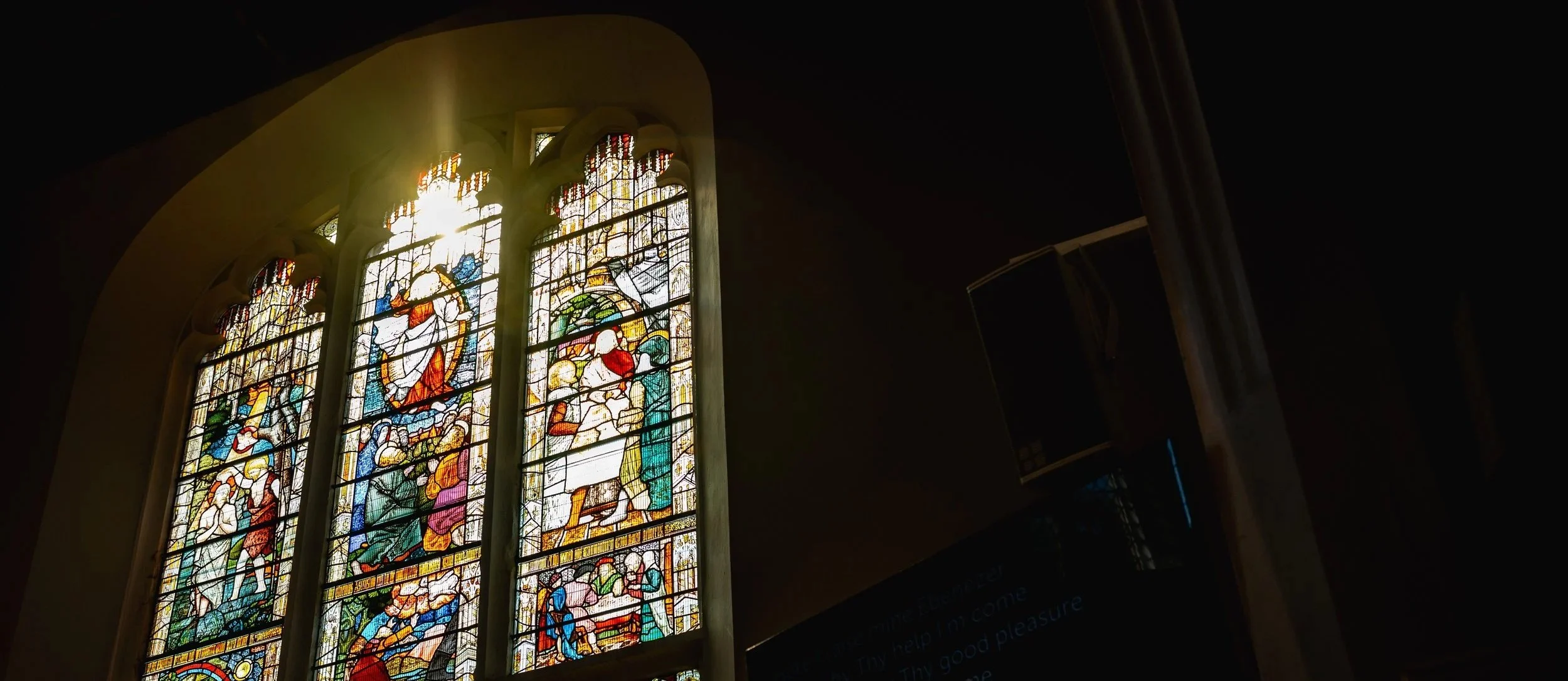 Sunlight shining through a colorful stained glass church window depicting religious figures.