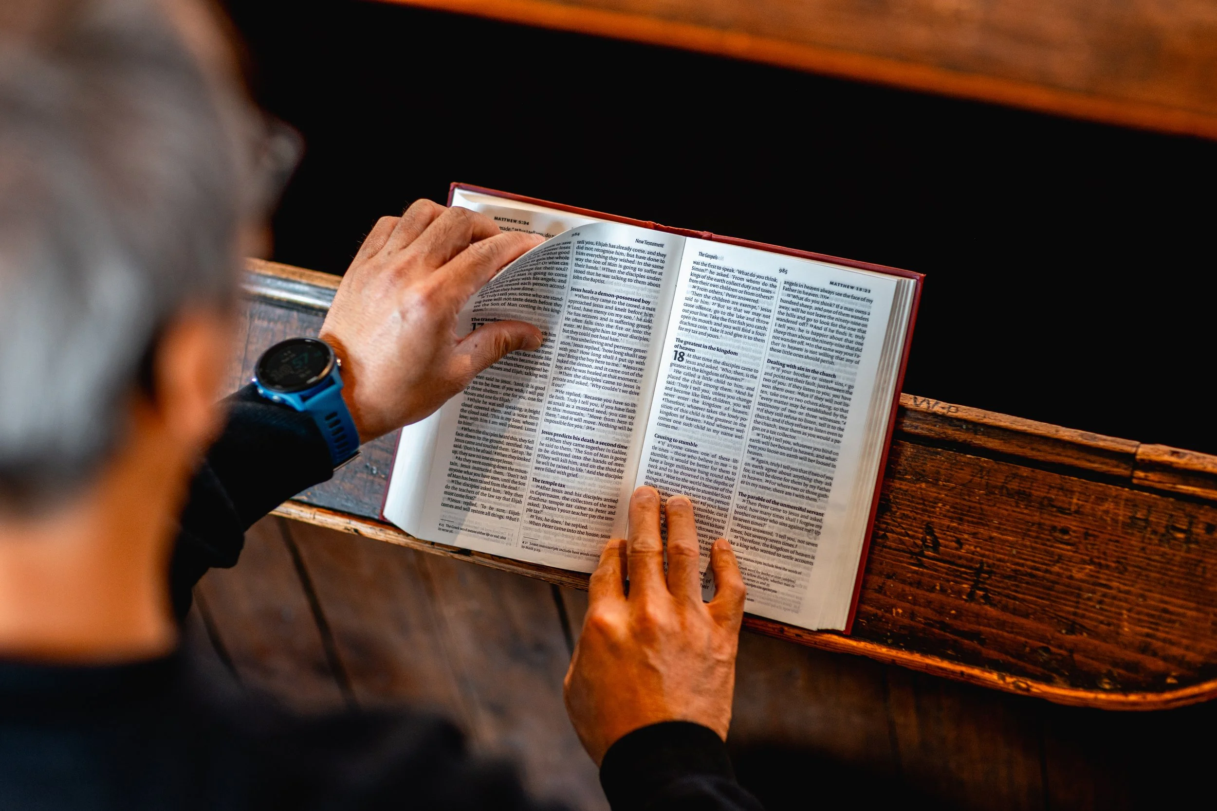 A person with a blue wristwatch reading a Bible.