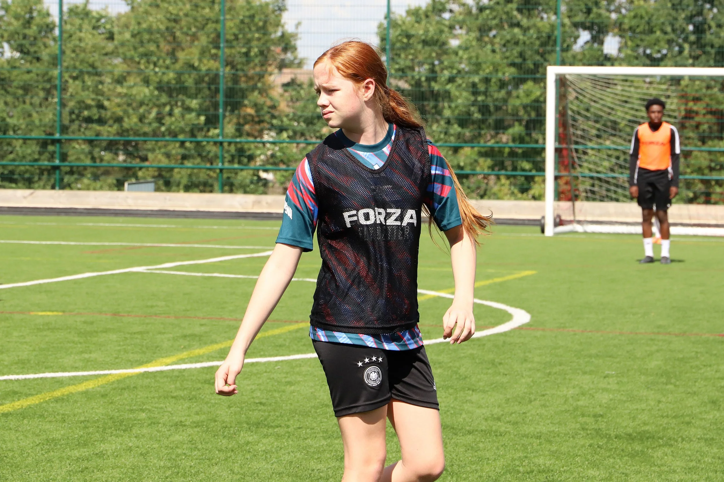 A young female  player with red hair in a ponytail looks to her left on a soccer field.