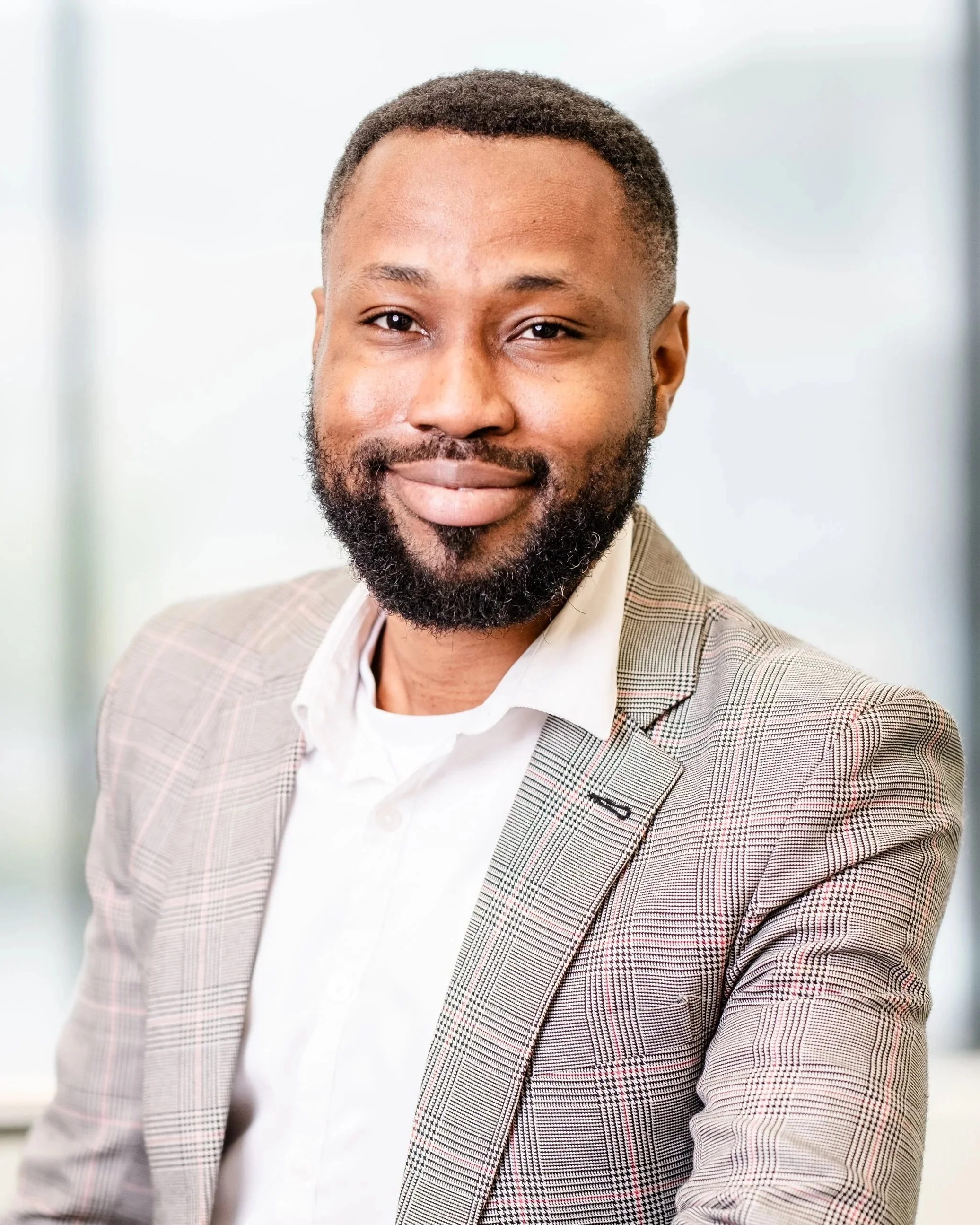 A young man in a white dress shirt and black tie standing in front of a beige wall.