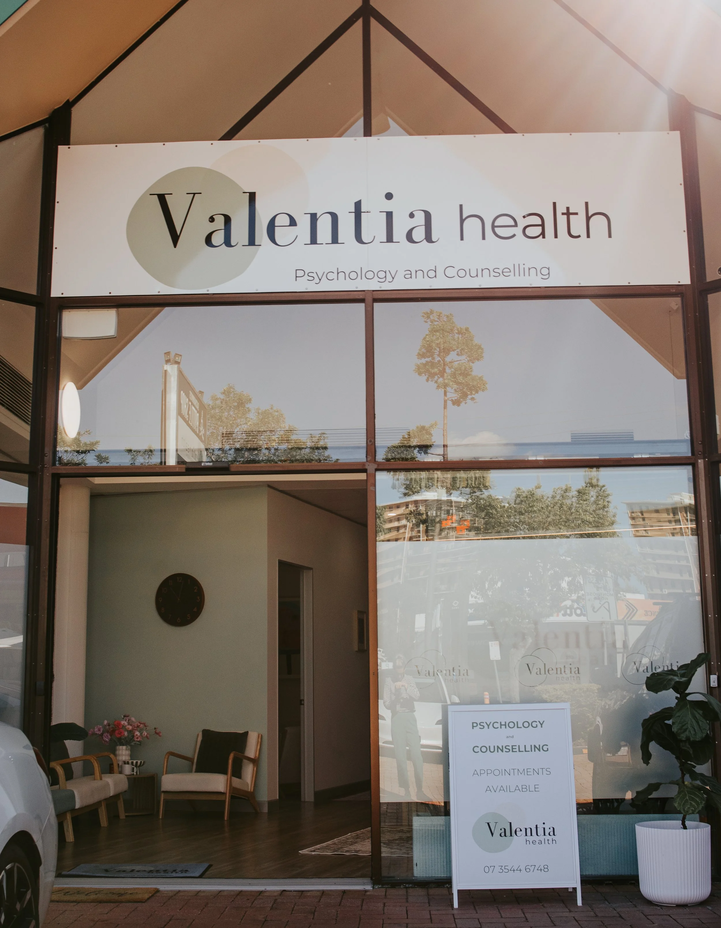 Sign for Valentia Health Psychology and Counselling, with interior seating visible and large windows reflecting trees and buildings outside.