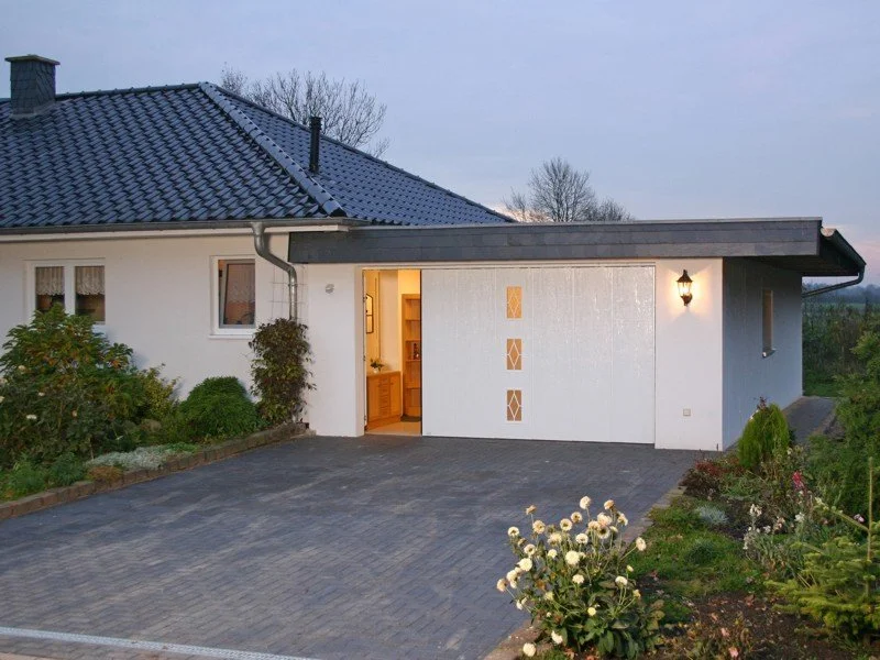 Weißes Einfamilienhaus mit Garagentor in der Abenddämmerung