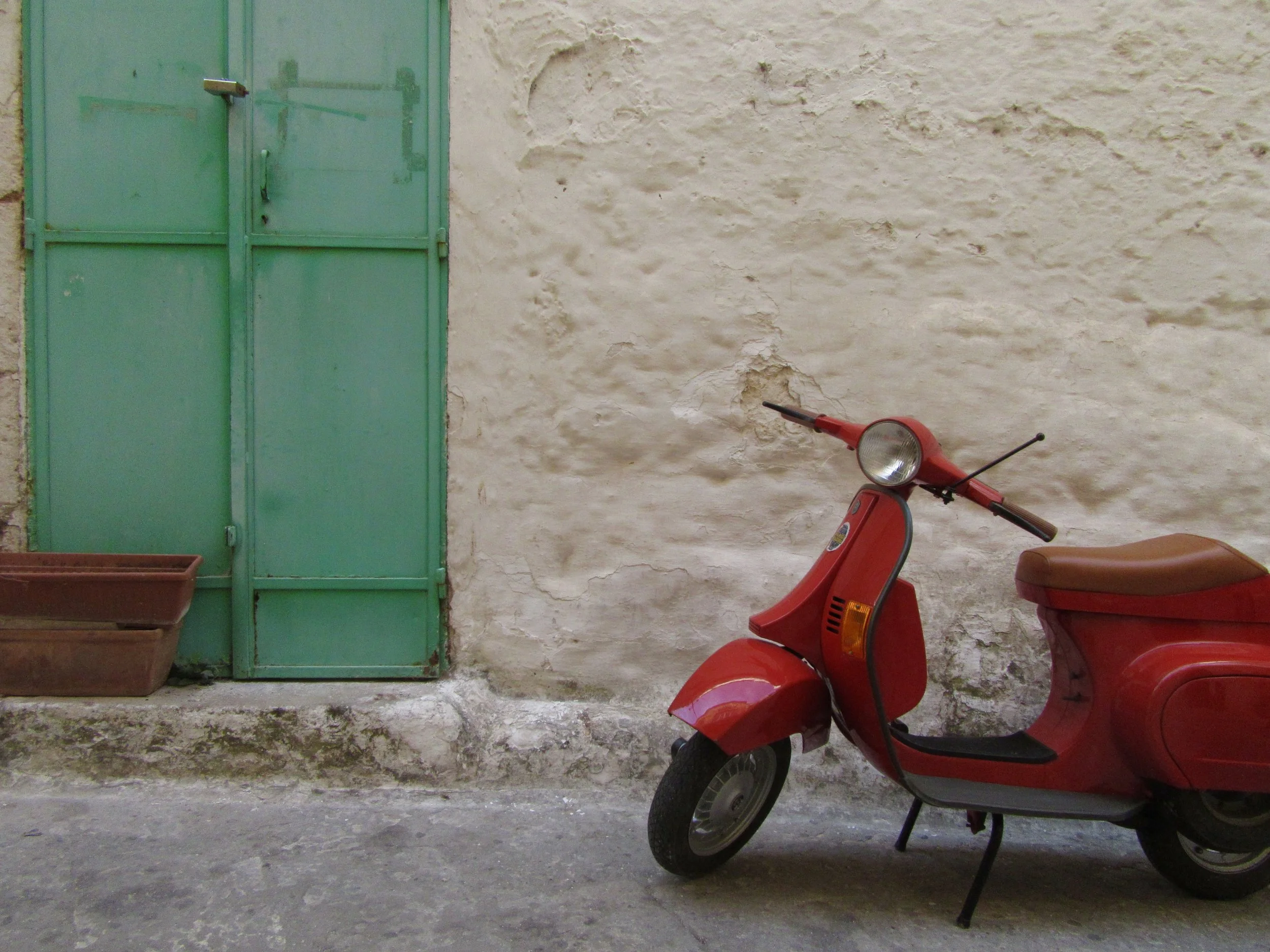 A red vespa against a stone wall and green doorway in Ostuni, Puglia.