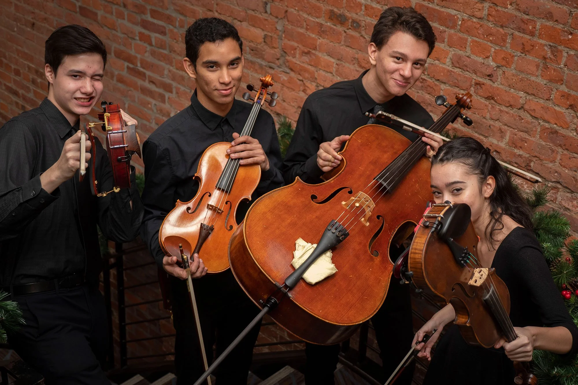 Young CMC violin players and a cello player smiling with funny poses while holding instruments.