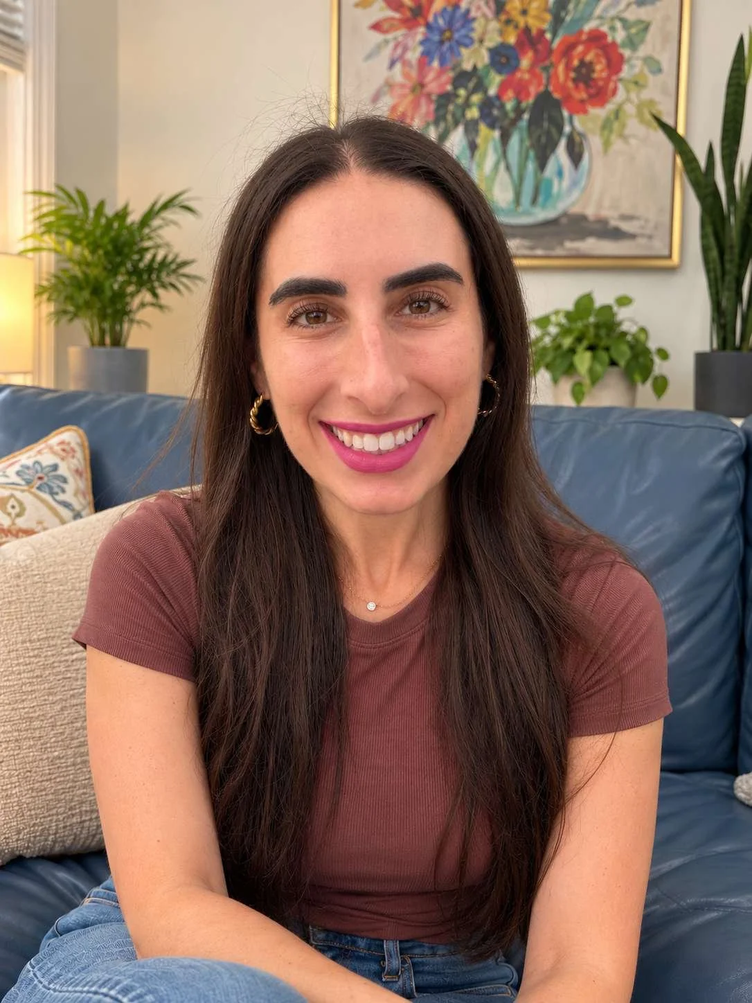 Lane, a woman with long brown hair, smiling, sitting on couch with colorful floral picture in background