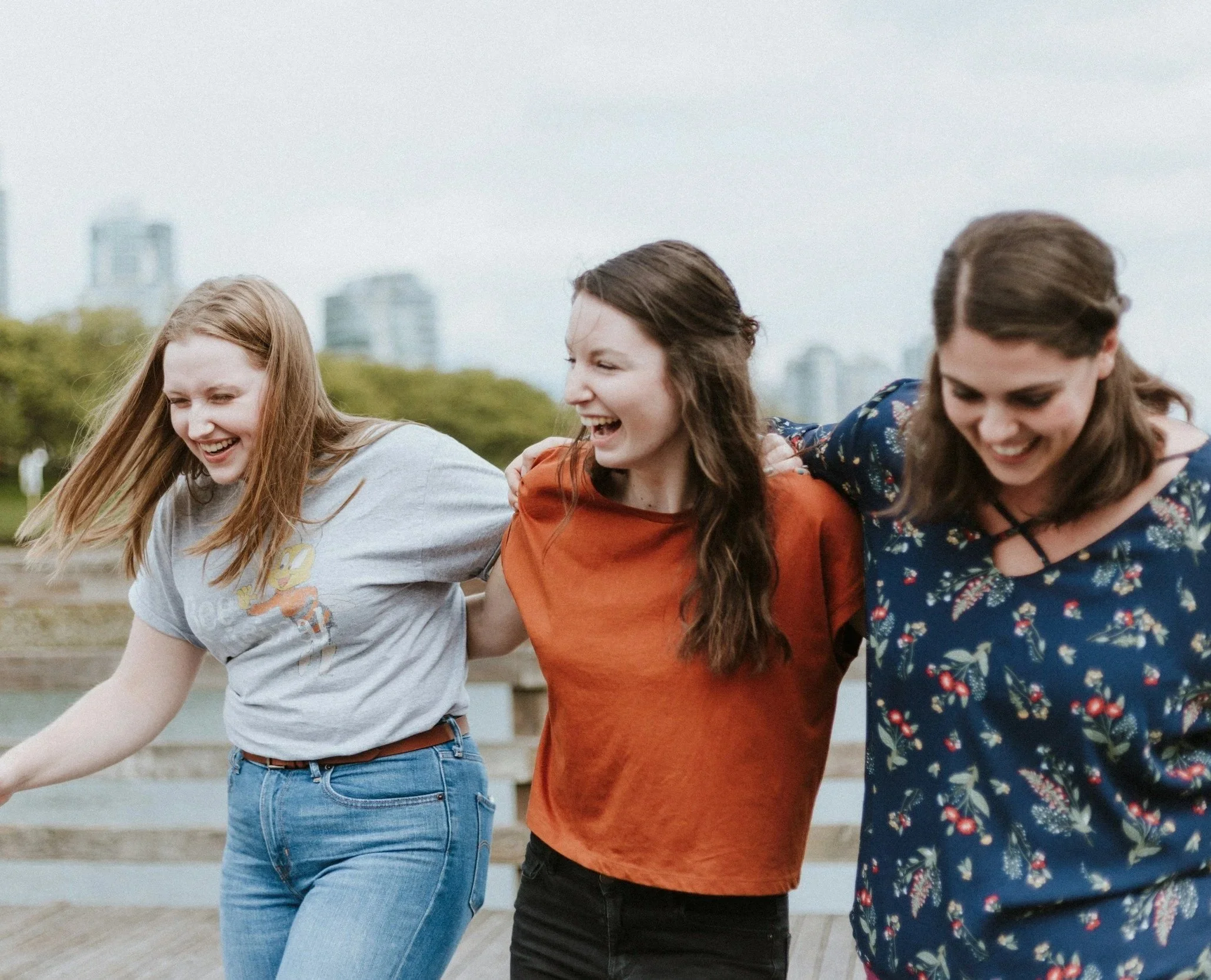 3 teen girls laughing with hands on eachothers shoulders