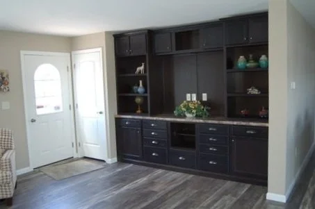 Living room with dark wooden built-in shelves and cabinets, decorative items, and a white front door.