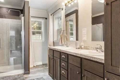 Modern bathroom with double vanity, granite countertop, dark wood cabinets, large mirror, shower with glass door, and tile flooring.