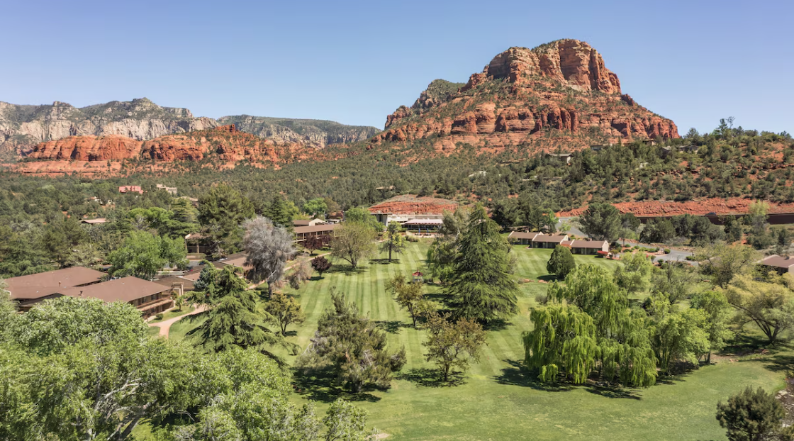 Scenic view of Sedona, Arizona, showing red rock formations, lush green landscaping, trees, and a residential area.