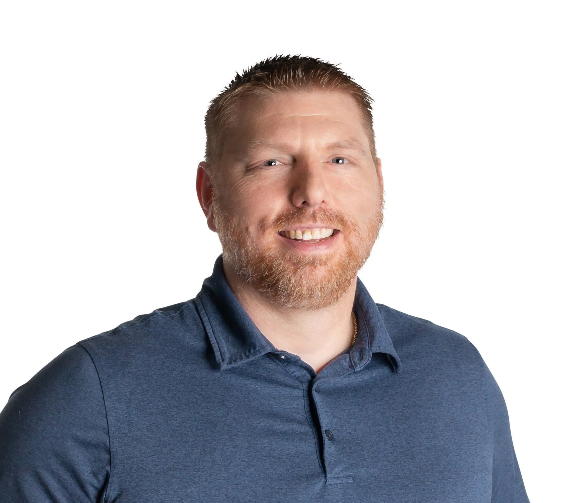 A man with short hair and a beard wearing a blue polo shirt, smiling, against a white background.