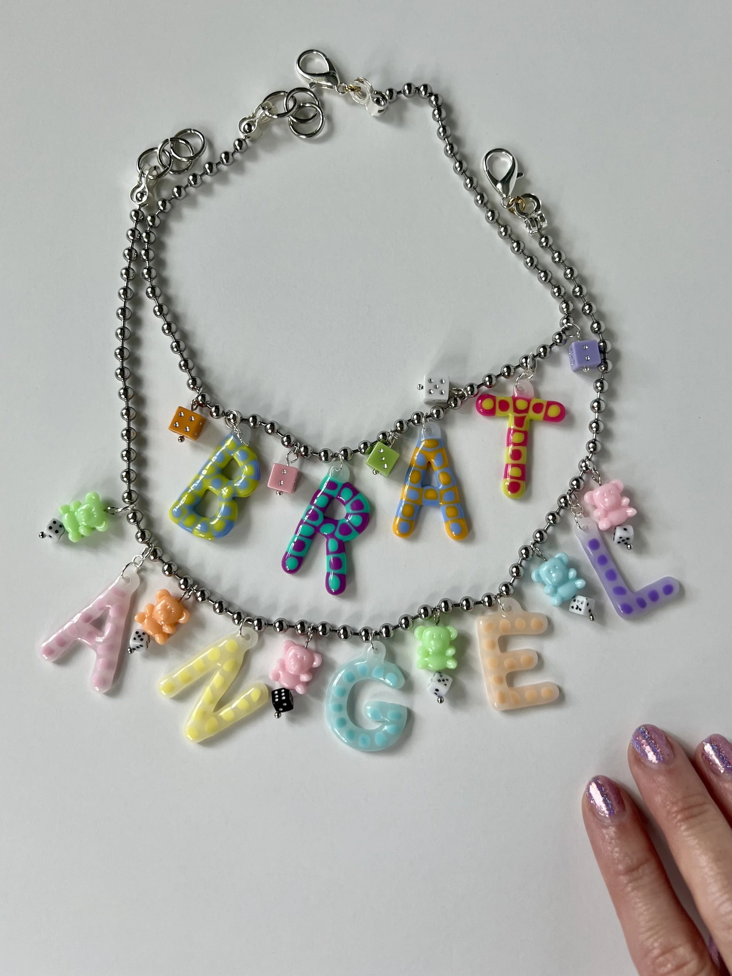 Colorful beaded necklace with alphabet and game piece charms, spelling "PARTY ALL" with a hand touching the bottom right corner.