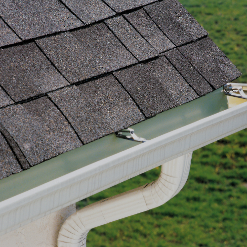 Close-up of asphalt shingle roof with metal gutter and downspout on a house.