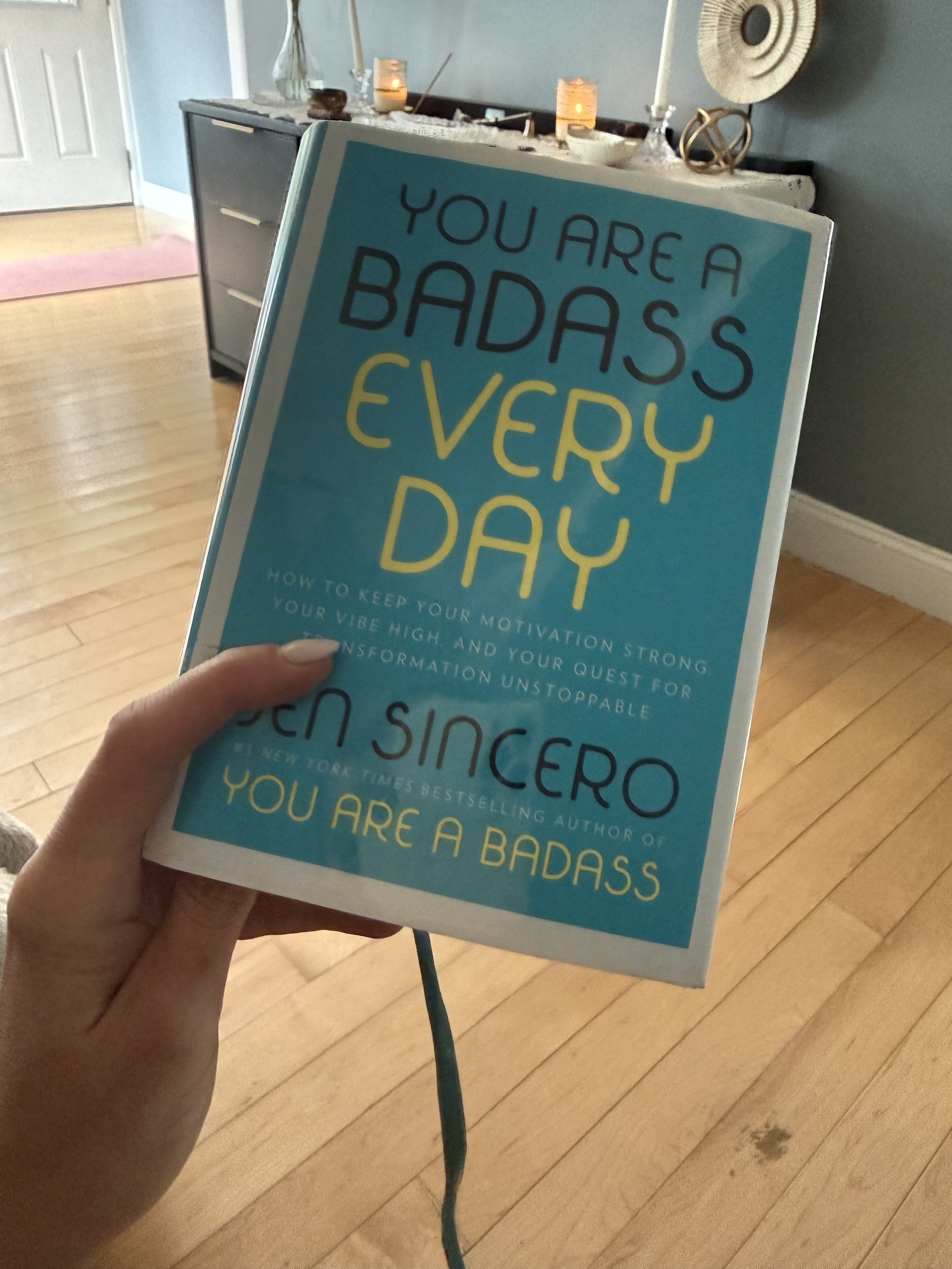 cyndi zaweski holding you are a badass everyday by jen sincero in her living room with candles in the background