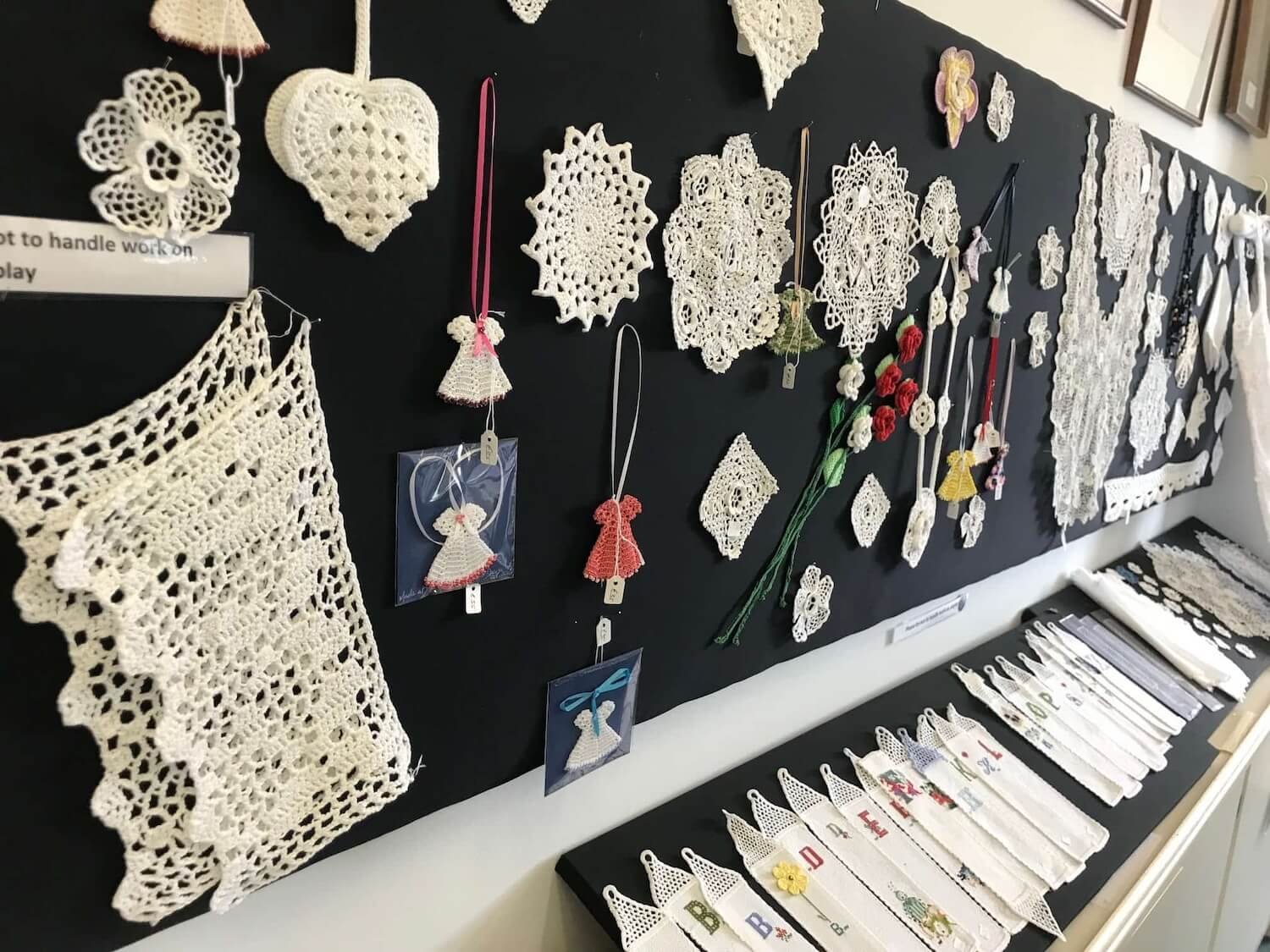 wall of irish lace samples mounted on a black background plus a shelf of lace bookmarks