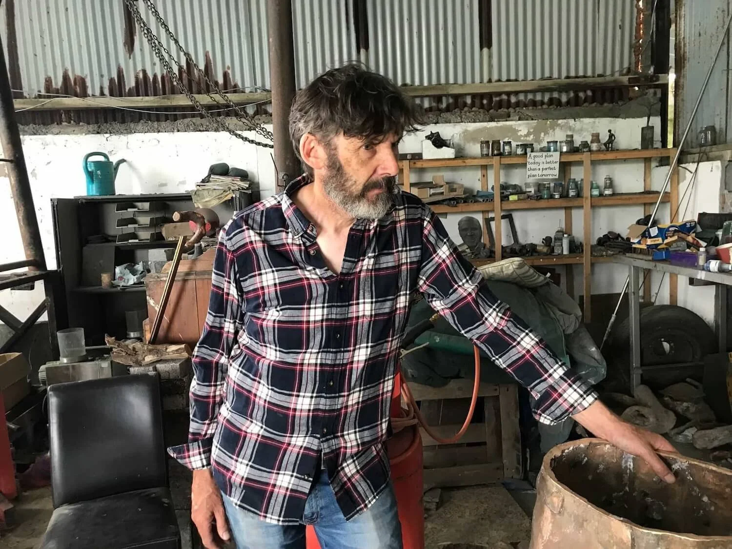 sculpter Seamus Connolly wearing a plaid shirt and standing in his workshop.
