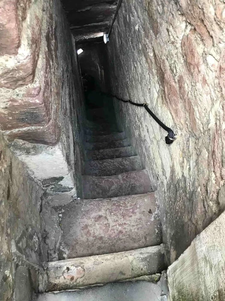 stone passageway with stairs and a rope railing going down into a dark corridor