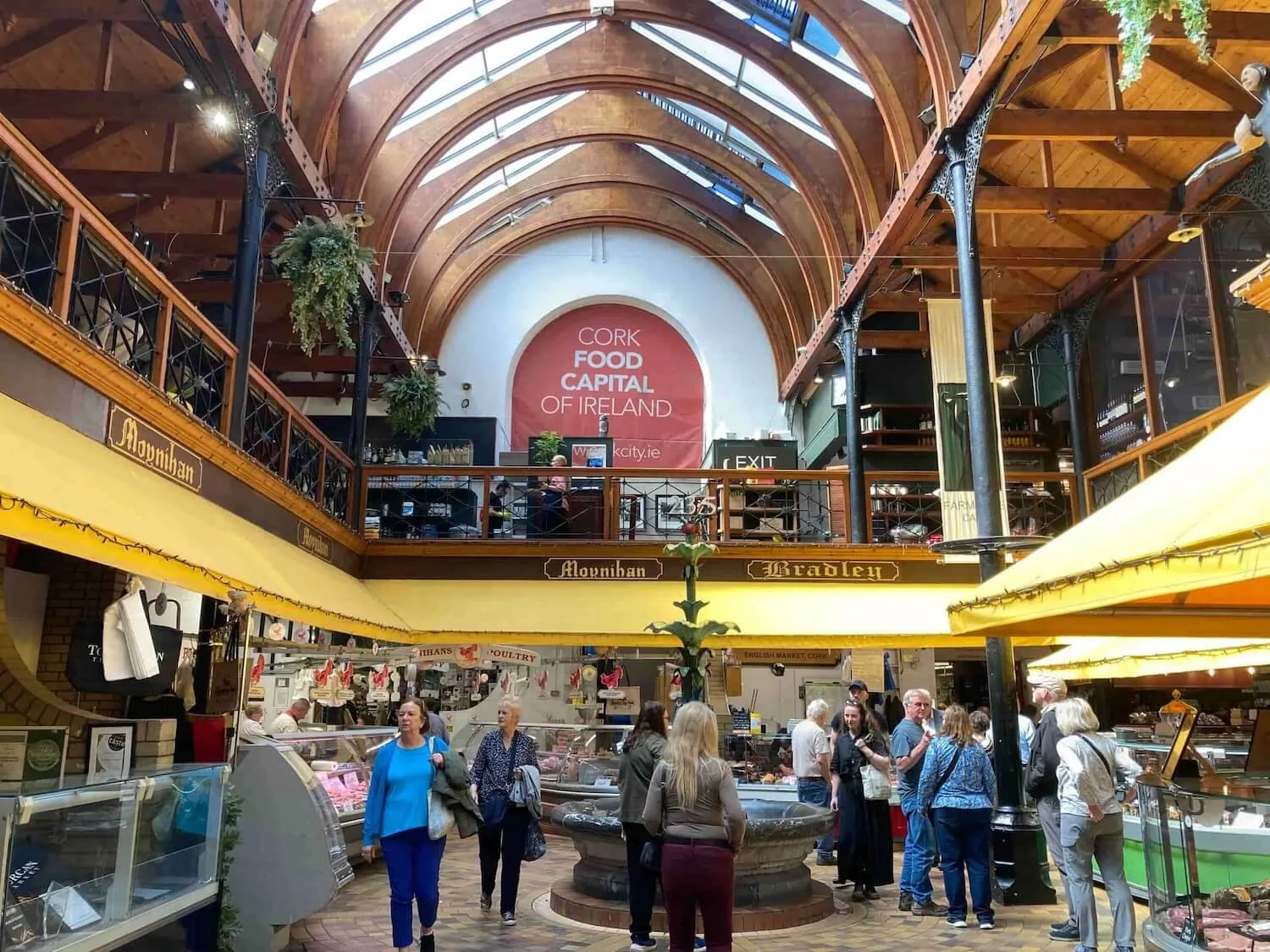 two stories of Cork Market with people waiting at vendors and arched wooden ceiling