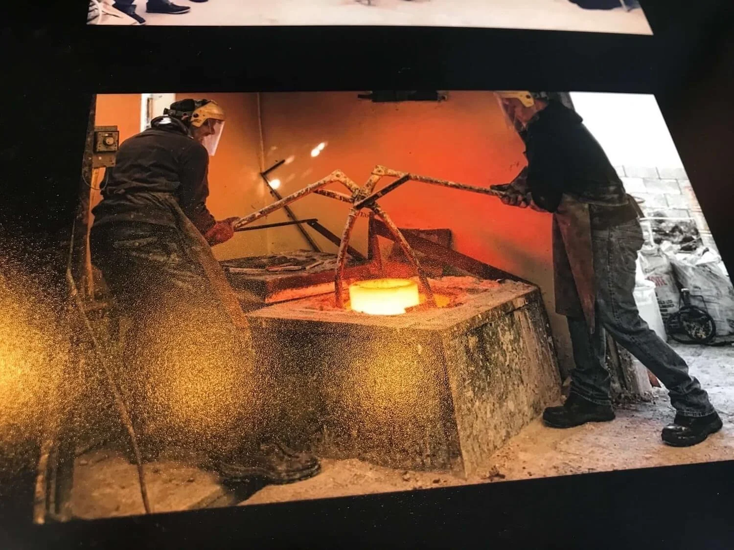 two sculptors lifting hot metal out of a fiery forge