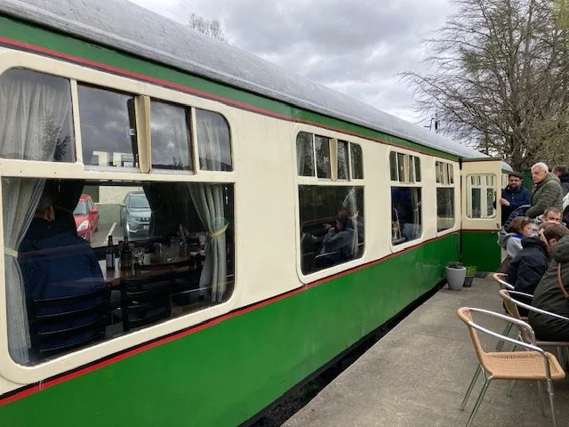 Green, cream and red Glenfinnan railway car cafe with chairs on the patio