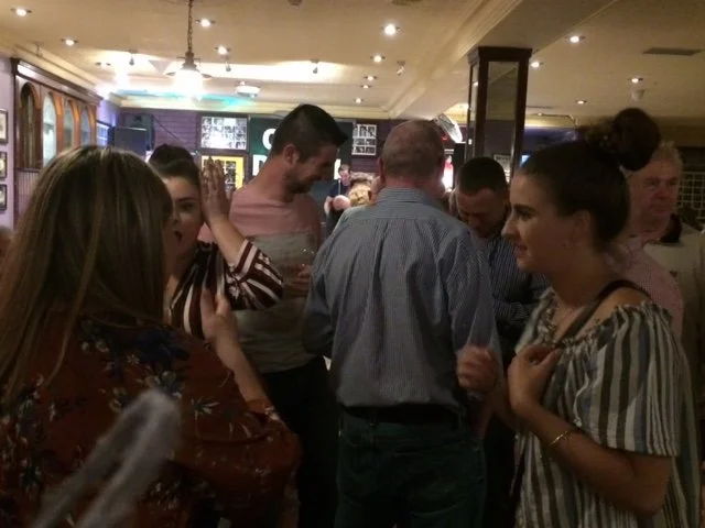 A group of people are socializing and talking inside a dimly lit pub