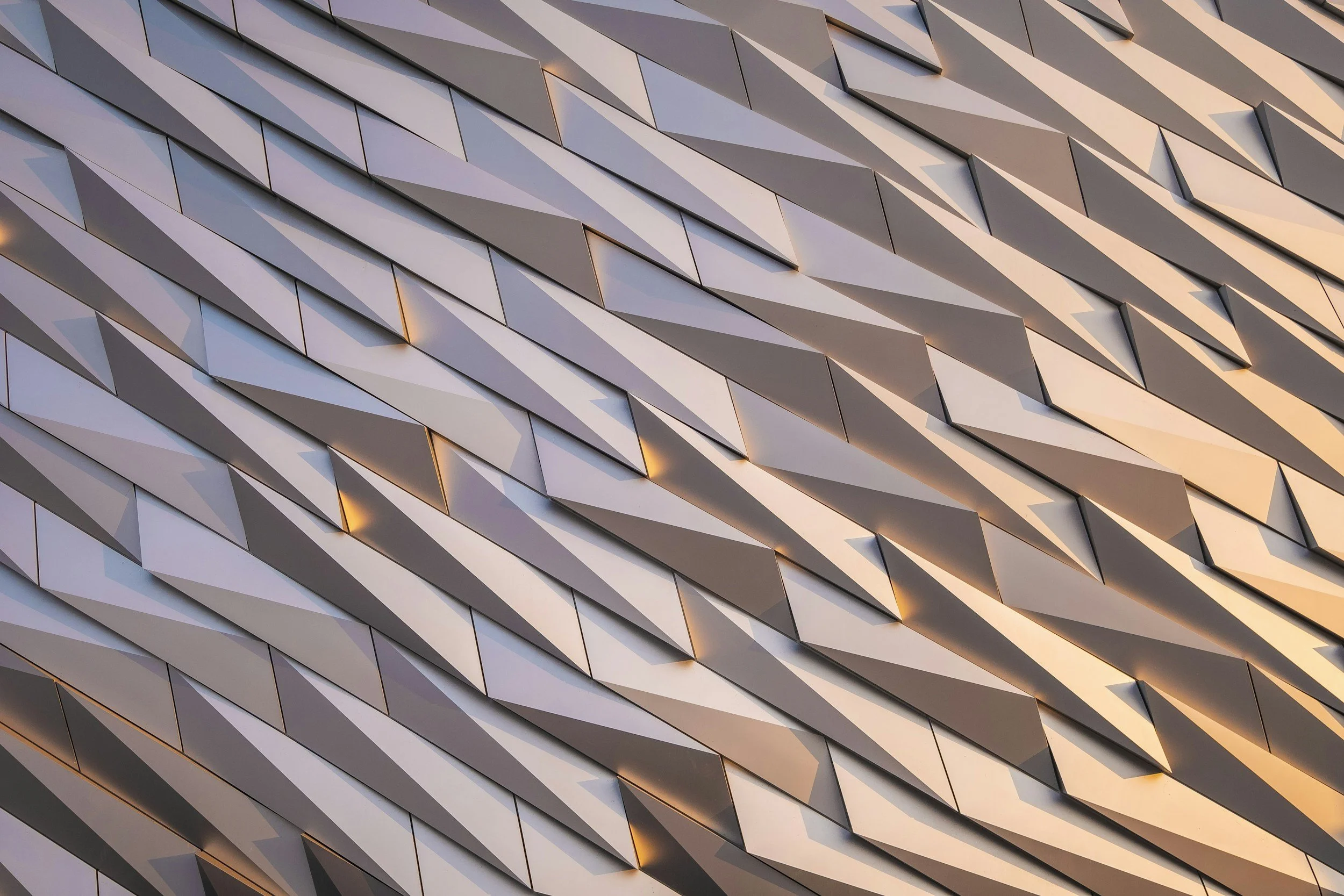Geometric architectural facade with angular and textured metallic panels, casting dynamic shadows.