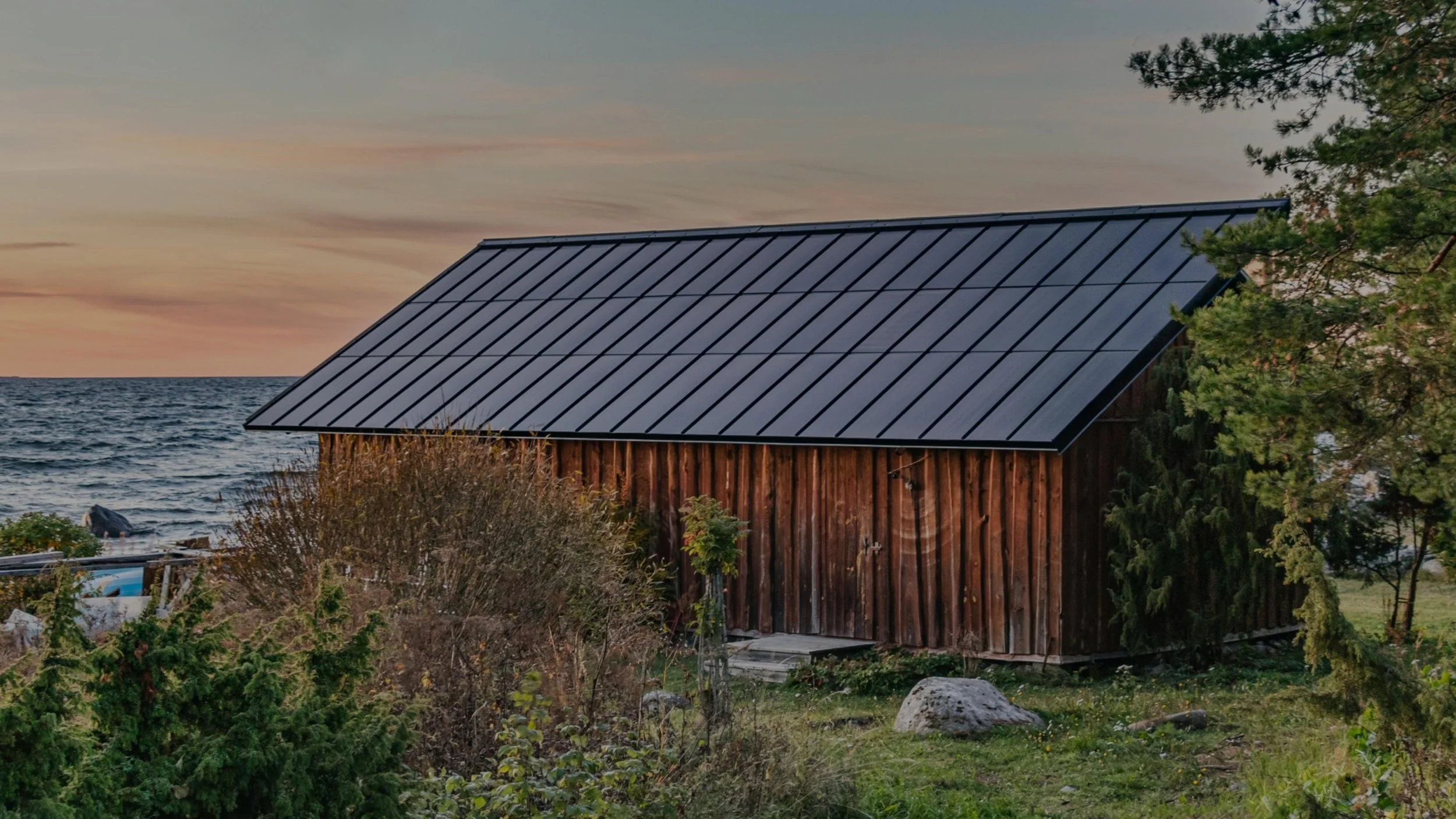 Wooden cabin with a solar panel roof near a lake at sunset.