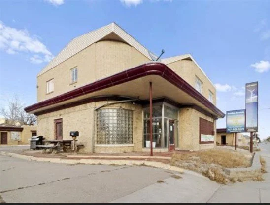 Historic Hotel The Rawlins Motor Inn hotel  with parking, parked cars, a sign for Rawlins Rentals, and a blue sky with clouds.