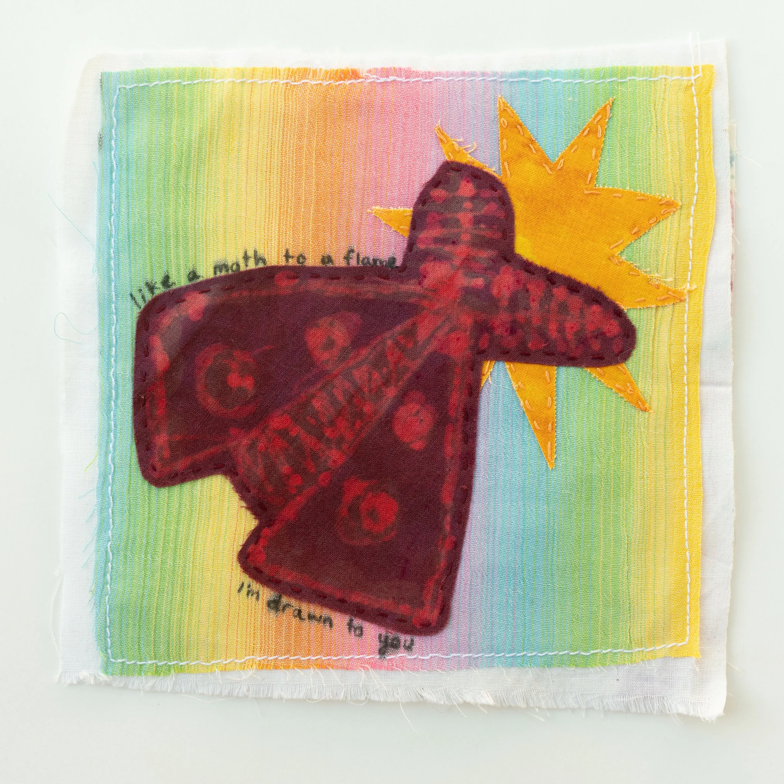Pastel blend rainbow background. An appliqued burgundy moth on top of a bright yellow star. The text 'like a moth to a flame I'm drawn to you" is arching over and under the moth.