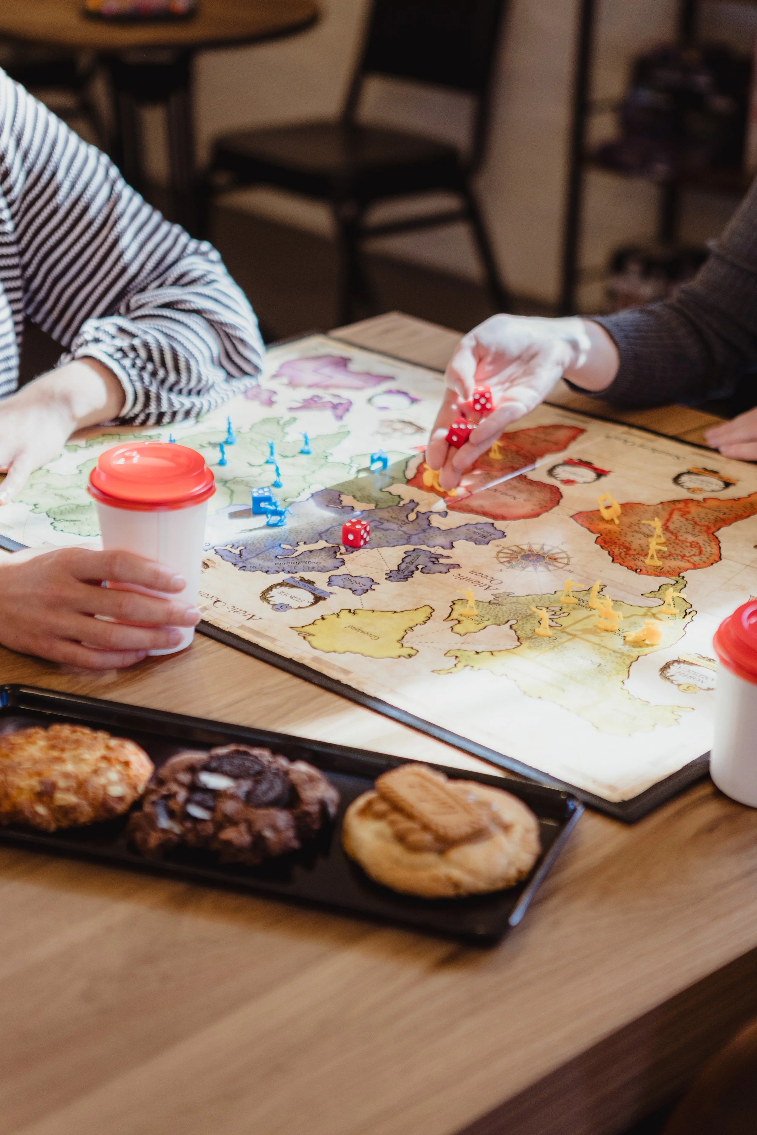 Two girls play a board game with coffees and cookies 
