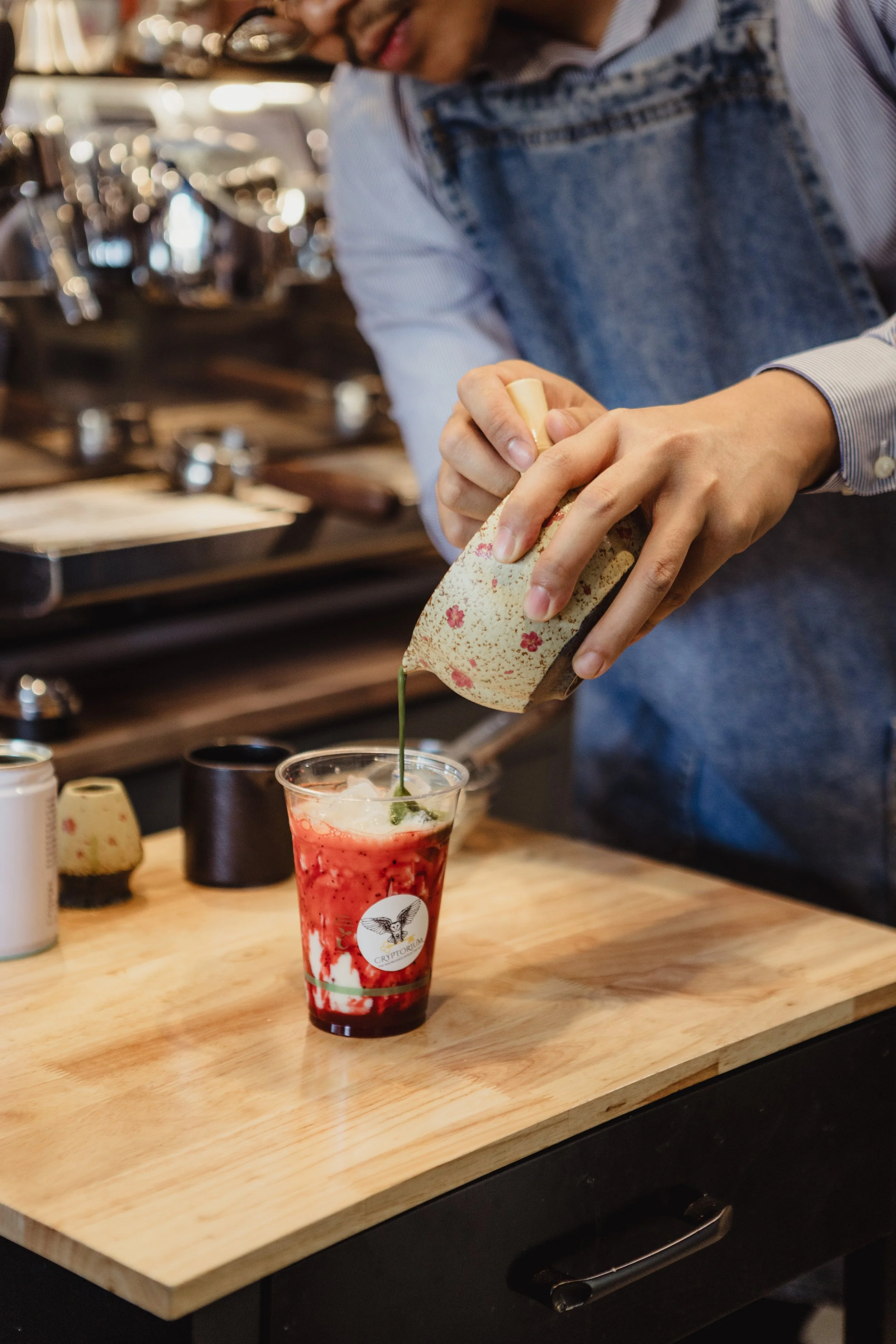 A strawberry matcha is being made on a bench, he matcha is being poured into the drink 