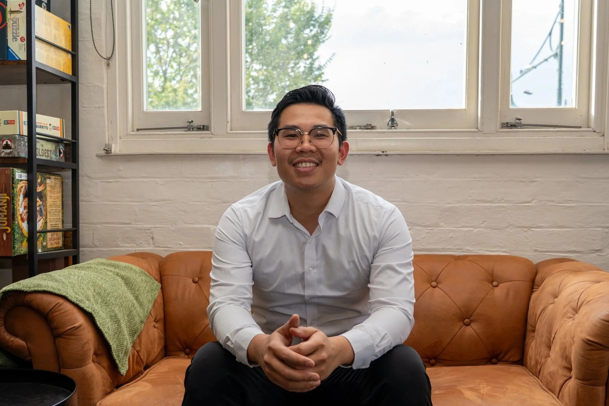 Smiling young man wearing sunglasses at the beach, holding a pine cone, with ocean and blue sky in the background.