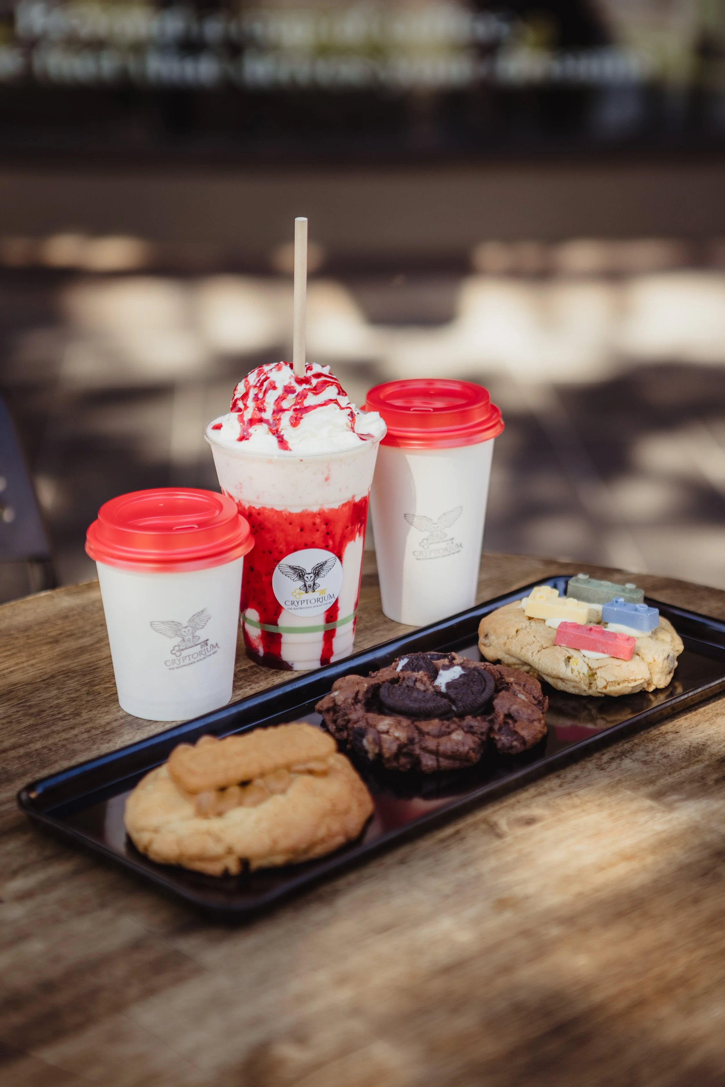 Coffees and strawberry milkshake lined up on a table. Three cookies on a plate . 