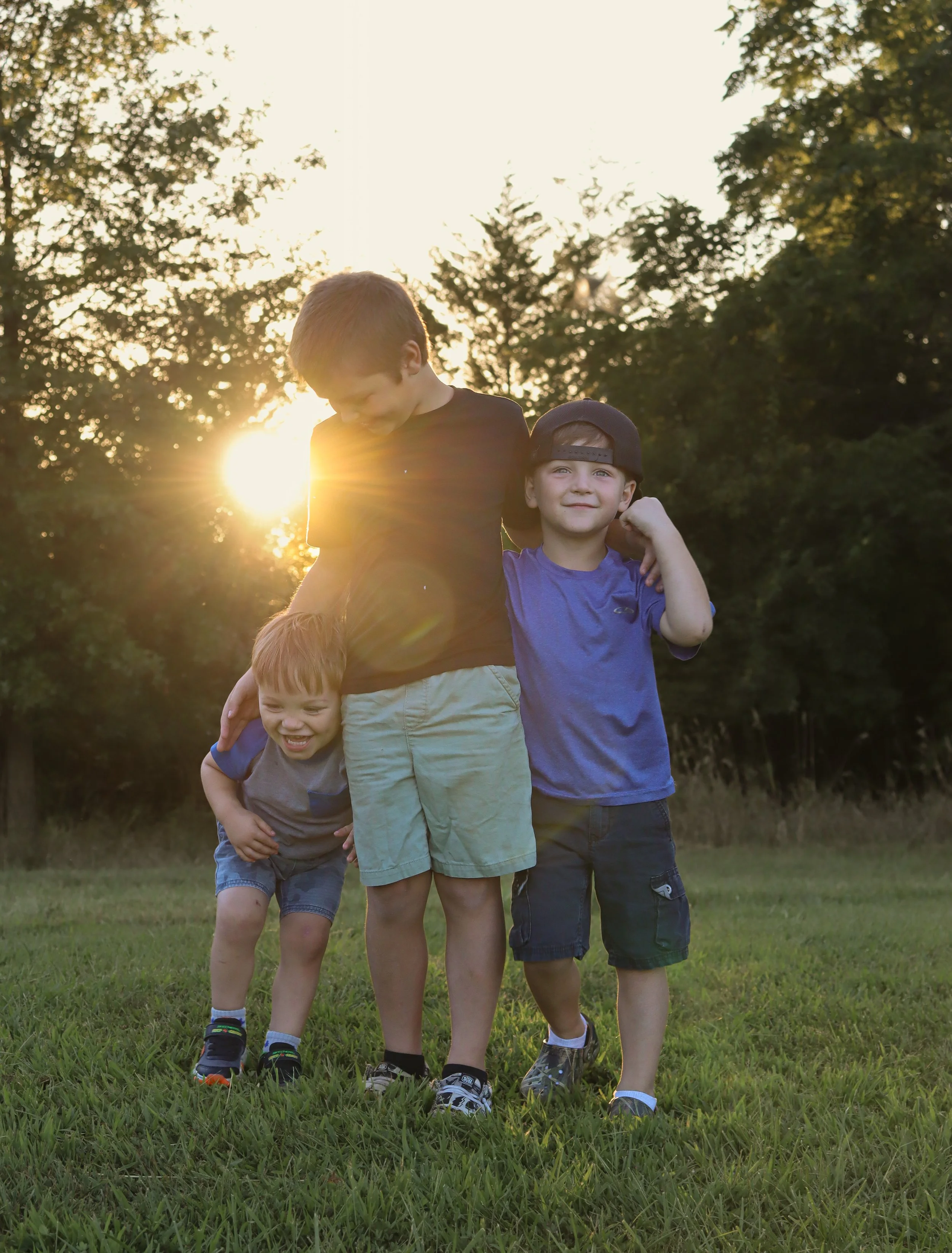 Four young boys playing outside on grass during sunset, with trees in the background.