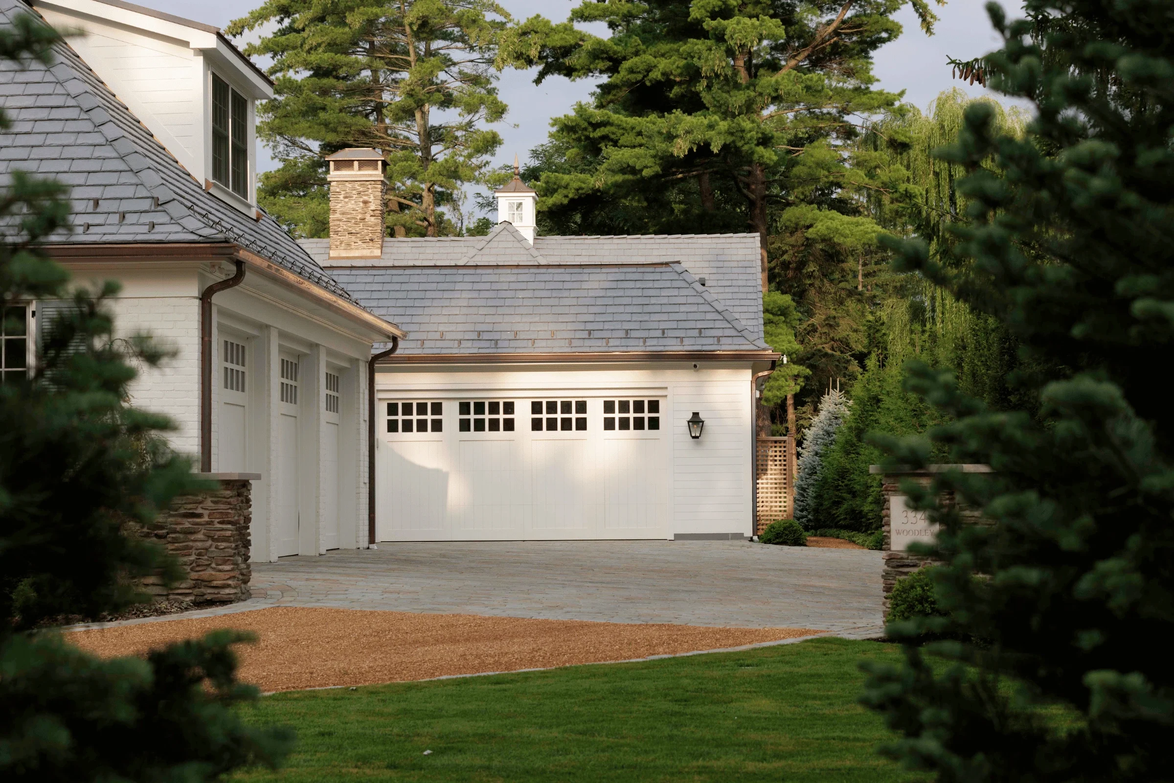 Cobblestone paver driveway and pea gravel courtyard in front of a white carriage-style garage with natural stone piers.