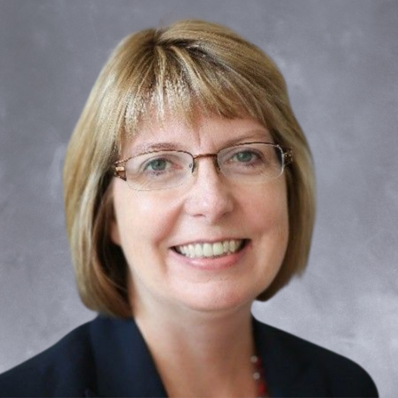 A woman with blonde hair, glasses, and a friendly smile, wearing a dark blazer, is posing for a professional headshot against a neutral background.
