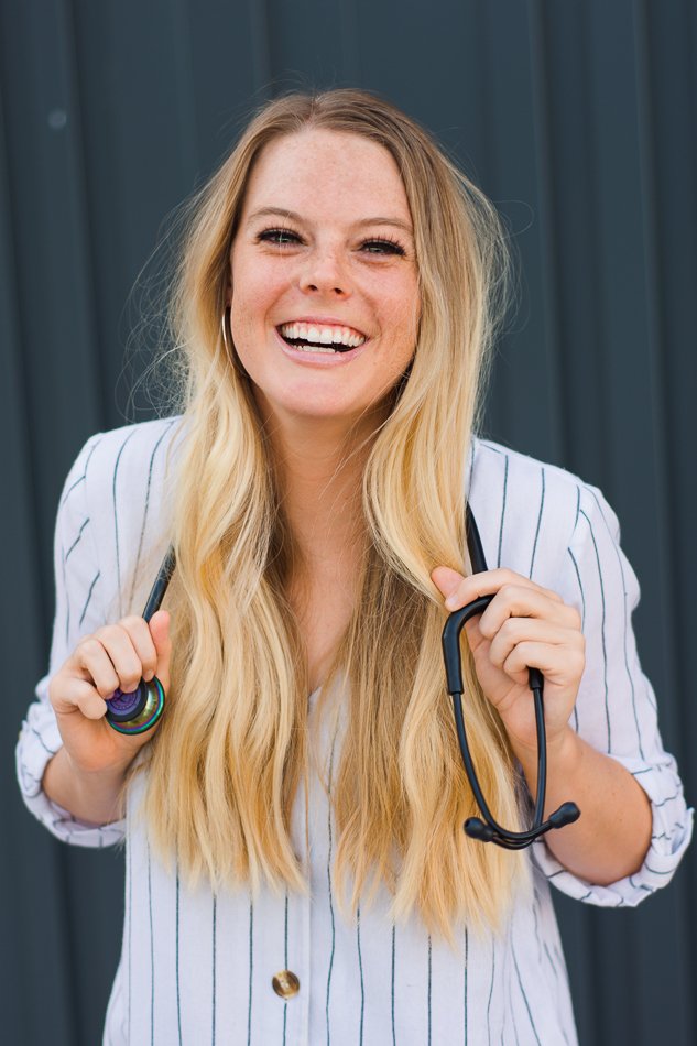 Smiling woman holding a stethoscope, wearing a striped shirt, with long blonde hair.