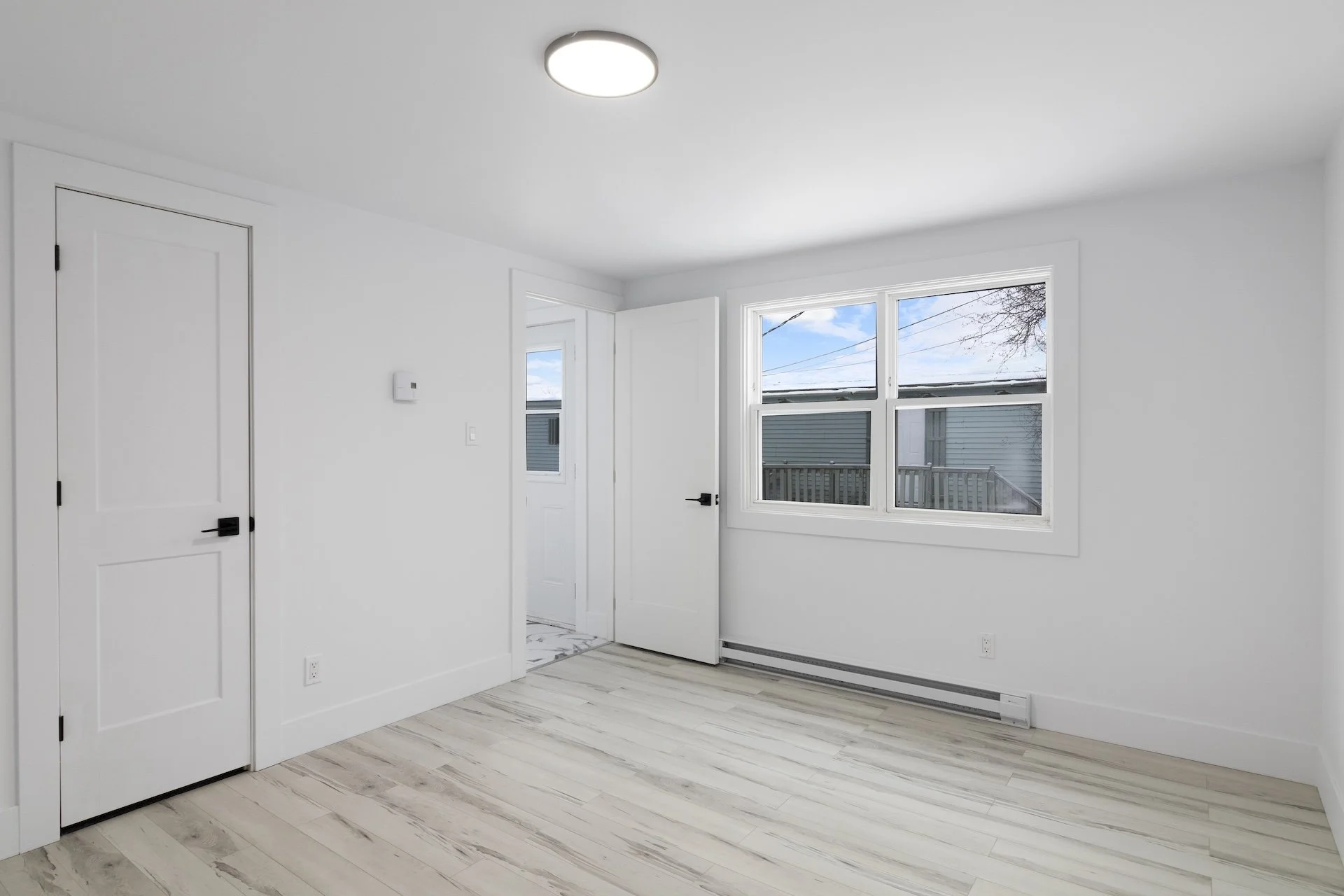 Empty room with white walls, a window showing the outside, and light-colored wood flooring.