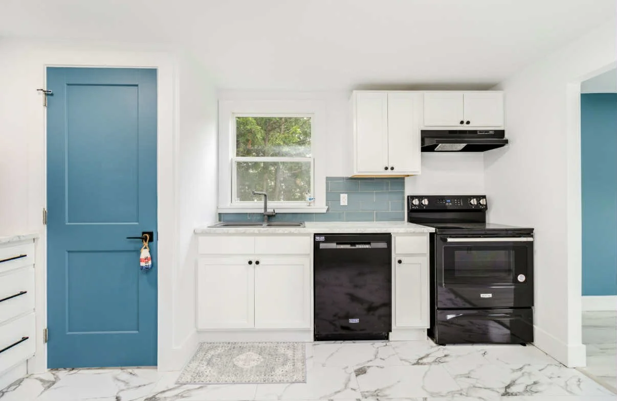 Kitchen with white cabinets, black appliances, blue backsplash, blue door, and marble floor.