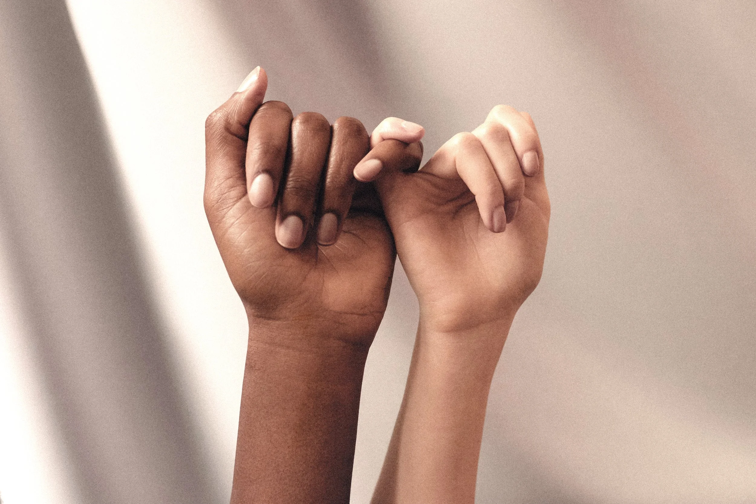 Two hands, one dark-skinned and one light-skinned, clasped together with fingers interlocked.
