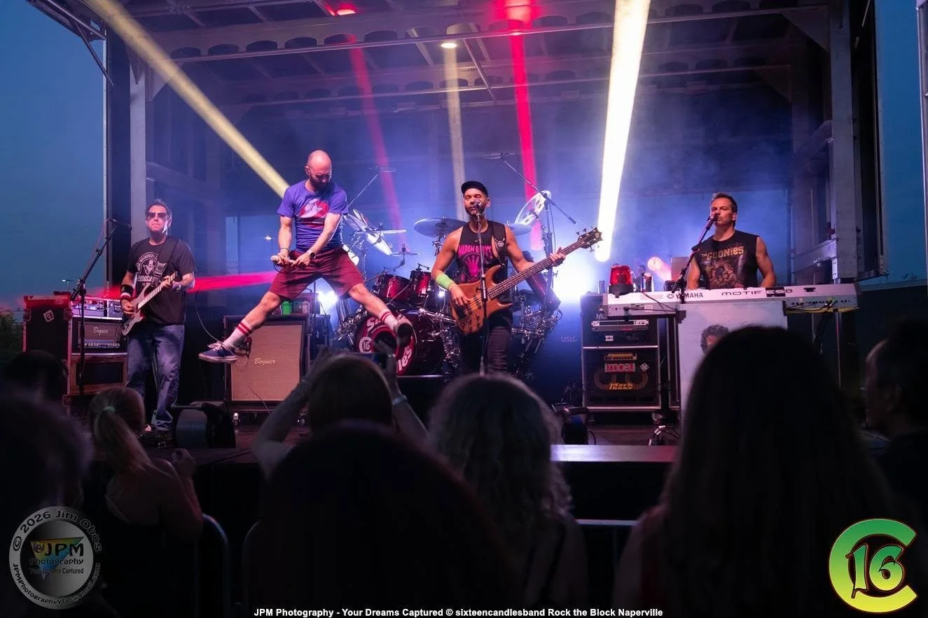 Band performing live on stage with colorful lights and smoke, audience watching in the foreground.