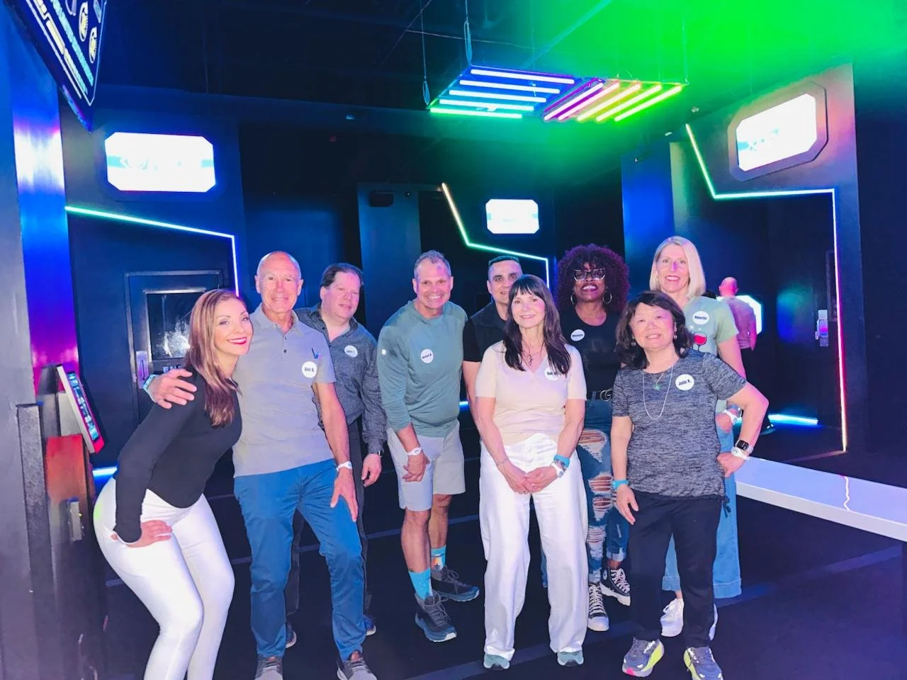 Group of nine people standing in a neon-lit room, smiling at the camera — Throwback Dating singles events Chicago over 50.
